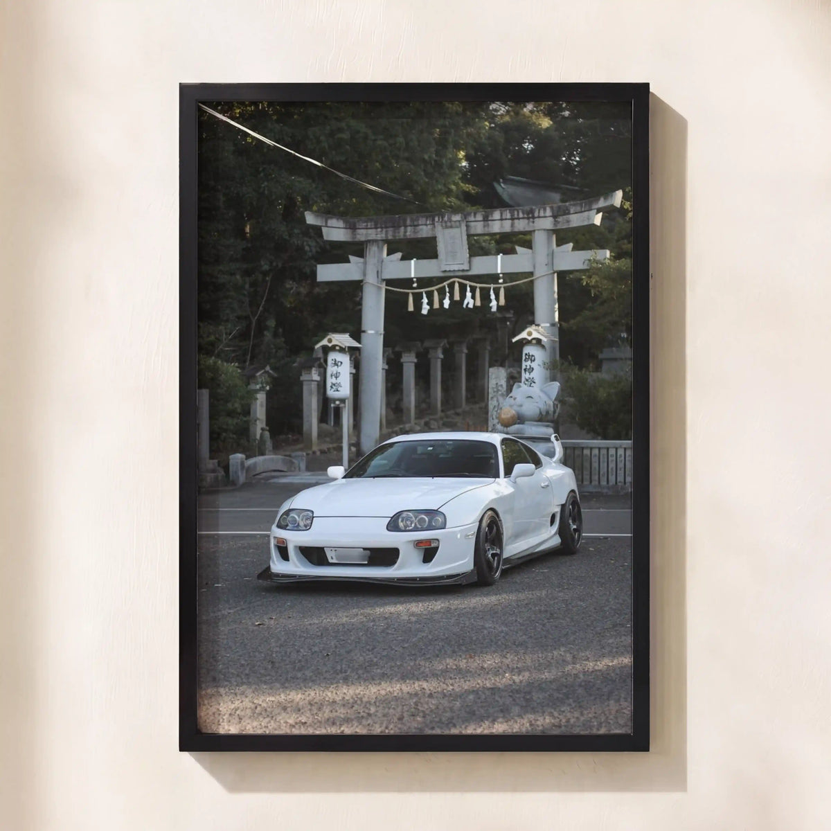 A framed vertical art print featuring a white sports car parked in front of a Japanese torii gate, displayed on a light beige wall.
