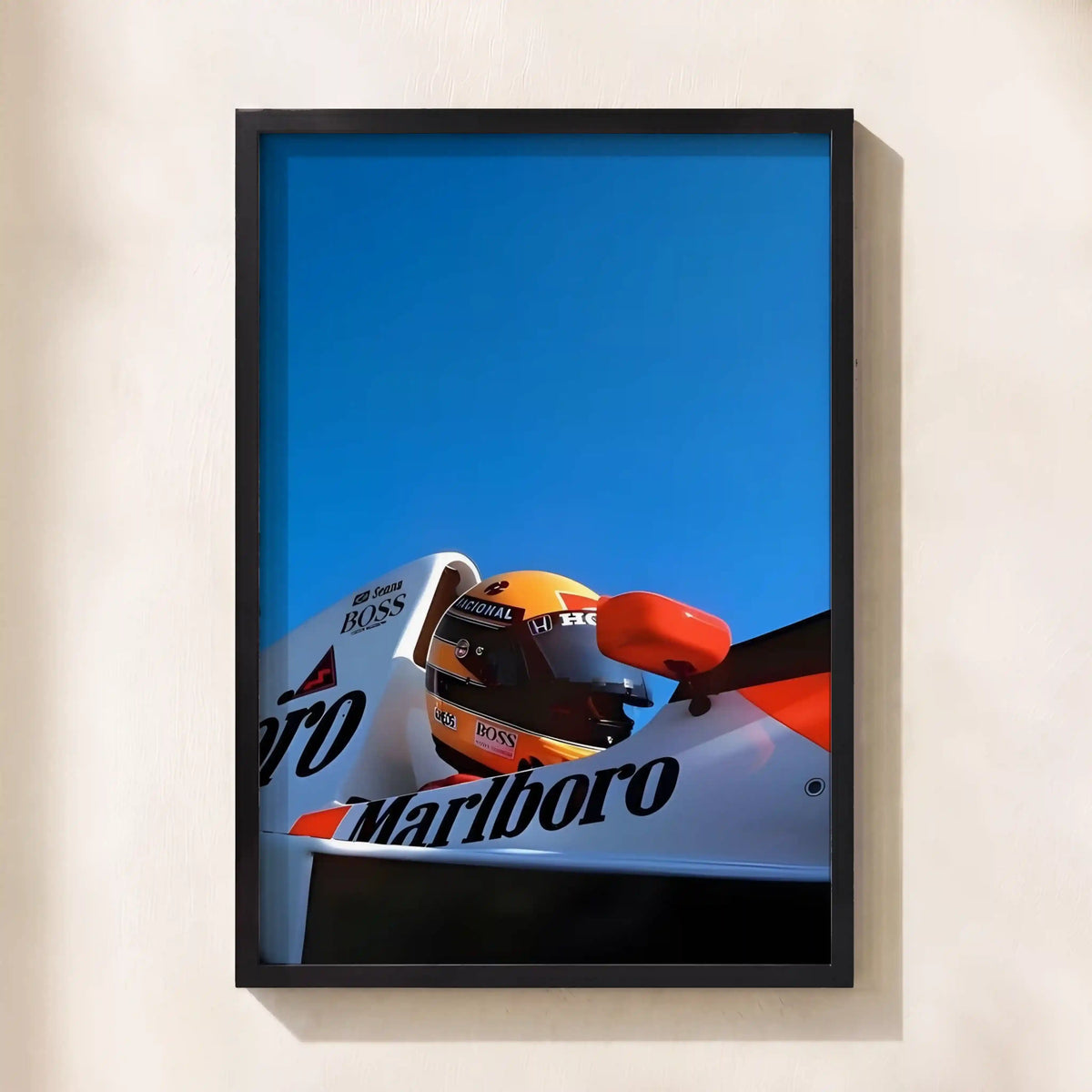 A framed art print of a Formula 1 race car driver wearing a helmet, featuring Marlboro and Booss branding against a bright blue sky, mounted on a beige wall.