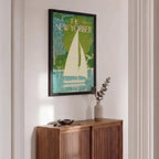 A framed New Yorker magazine cover featuring a sailboat illustration in green, teal, cream, and blue tones, displayed on a white wall above a wooden credenza in a styled interior.