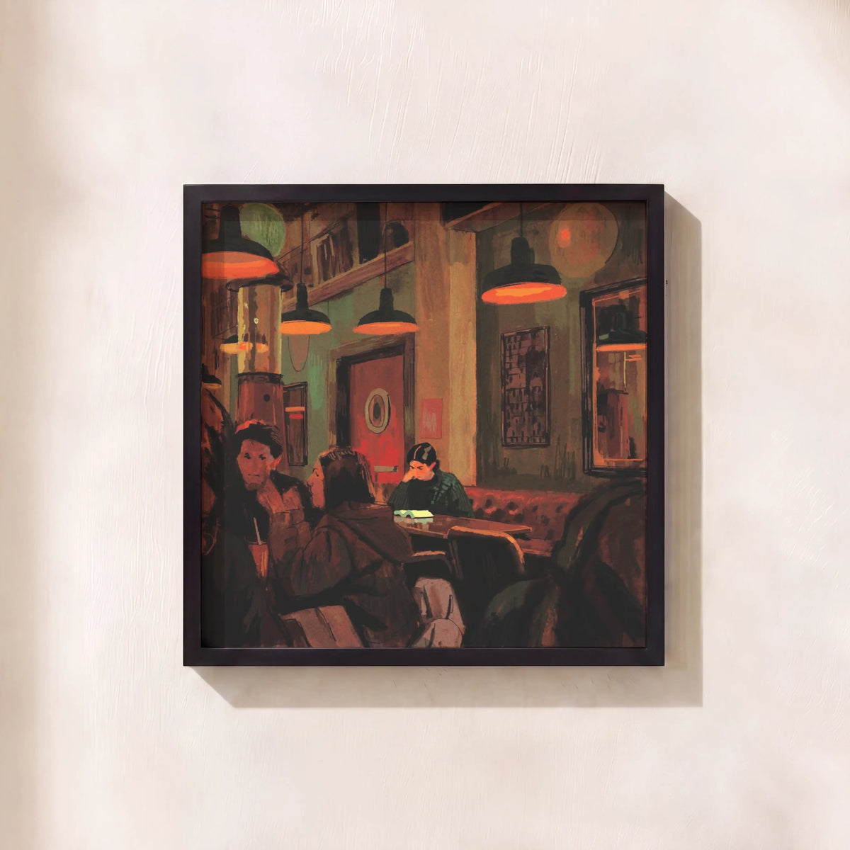 A framed art print depicting a cozy, warmly lit cafe interior with patrons and hanging pendant lights, mounted on a textured off-white wall.