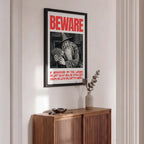 Framed poster with 'Beware' text above a wooden cabinet.