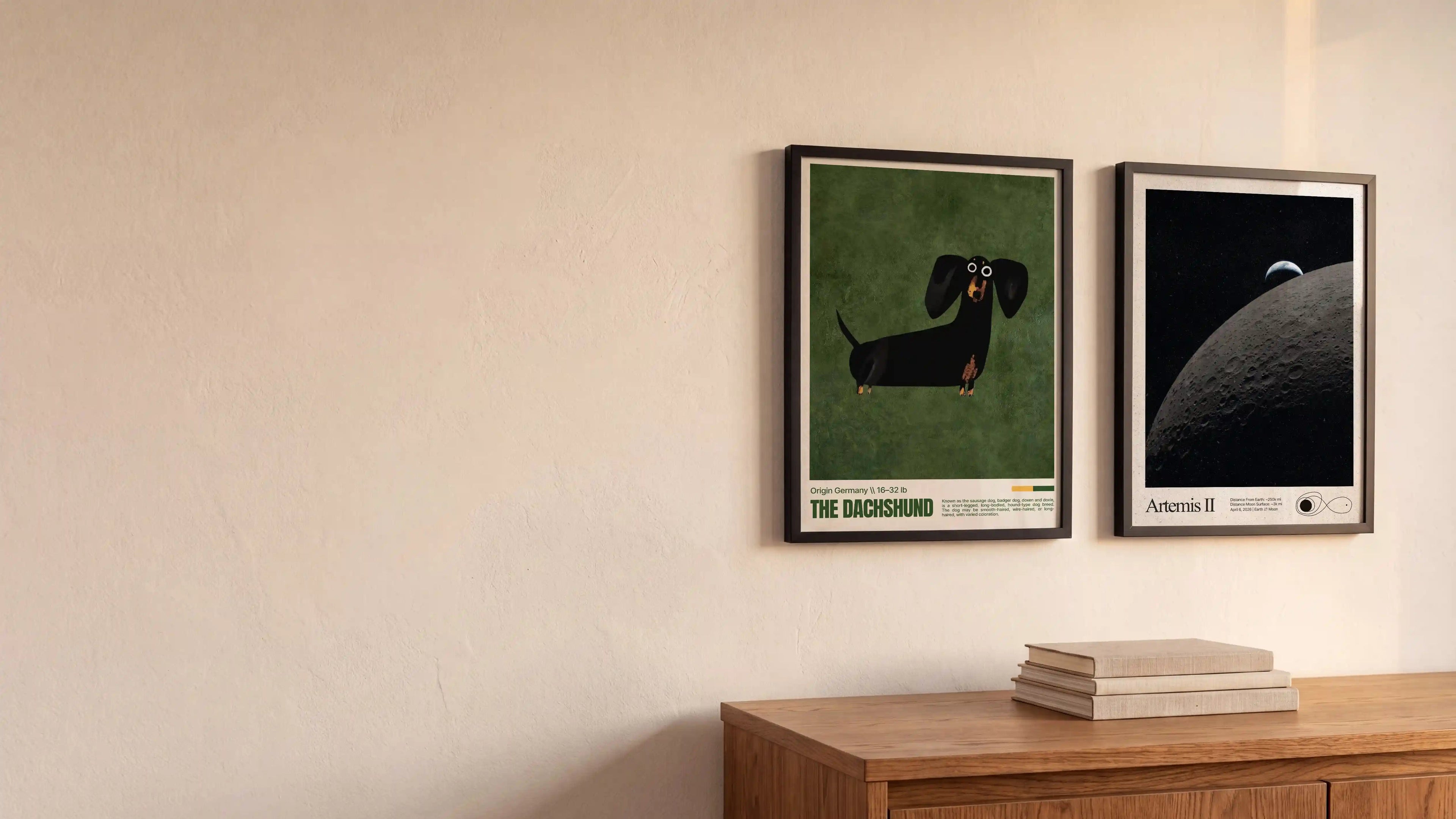 Two framed minimalist art prints hanging on a beige wall above a wooden cabinet. The left print features a black dachshund on a green background with the text 'THE DACHSHUND' at the bottom.