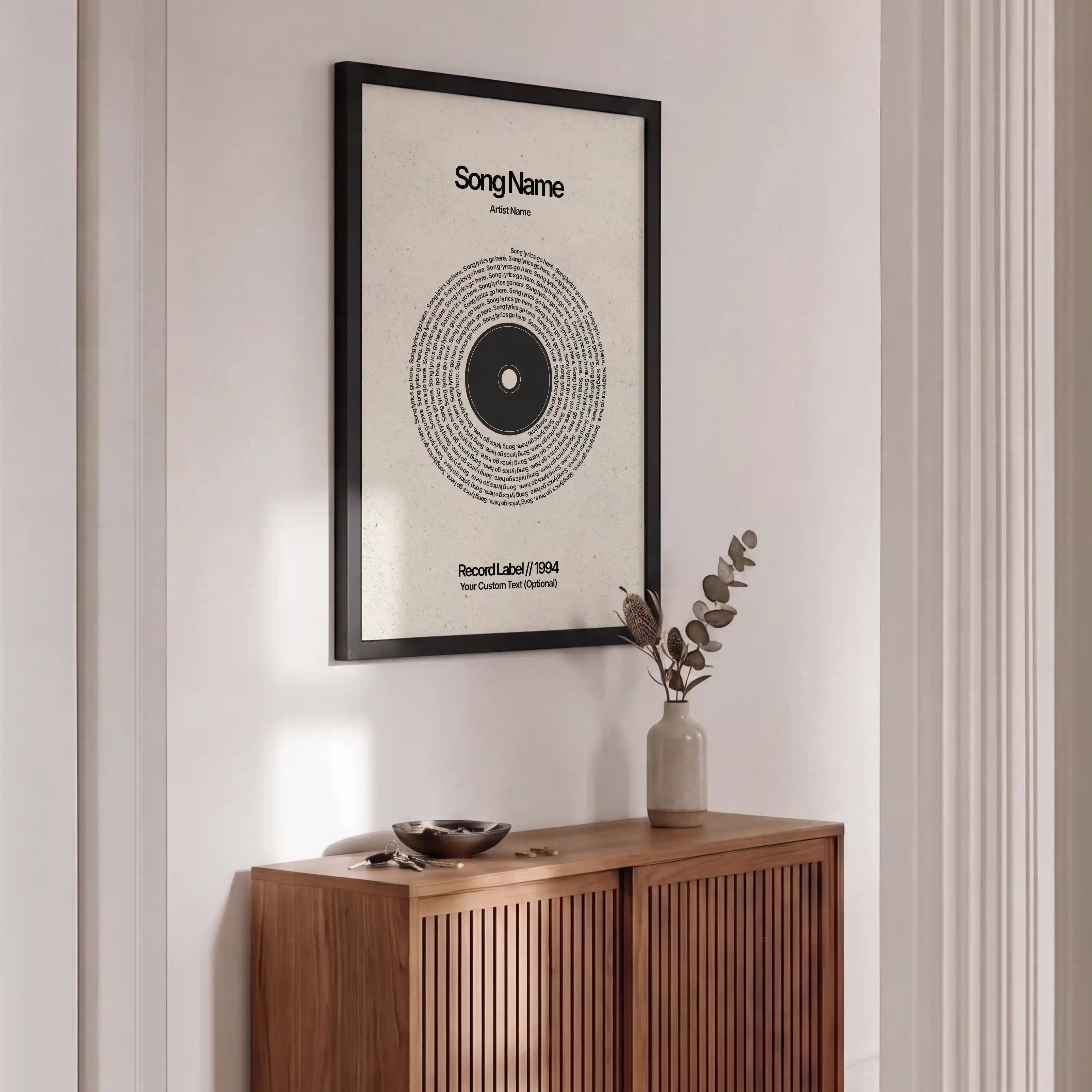A framed minimalist music poster with a vinyl record design hangs on a white wall above a wooden credenza in a modern interior setting.